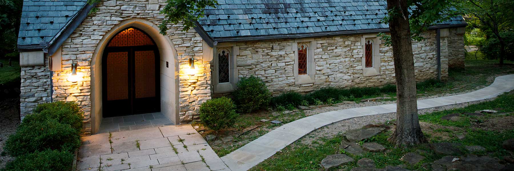 Curving grassy path in front of a limestone building with yellow scones at dusk.