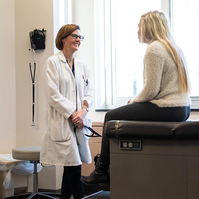 A doctor speaks with a female student on an exam table at the Health Center.