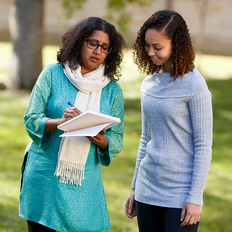 A female instructor writes on a notebook to explain something to a student next to her.